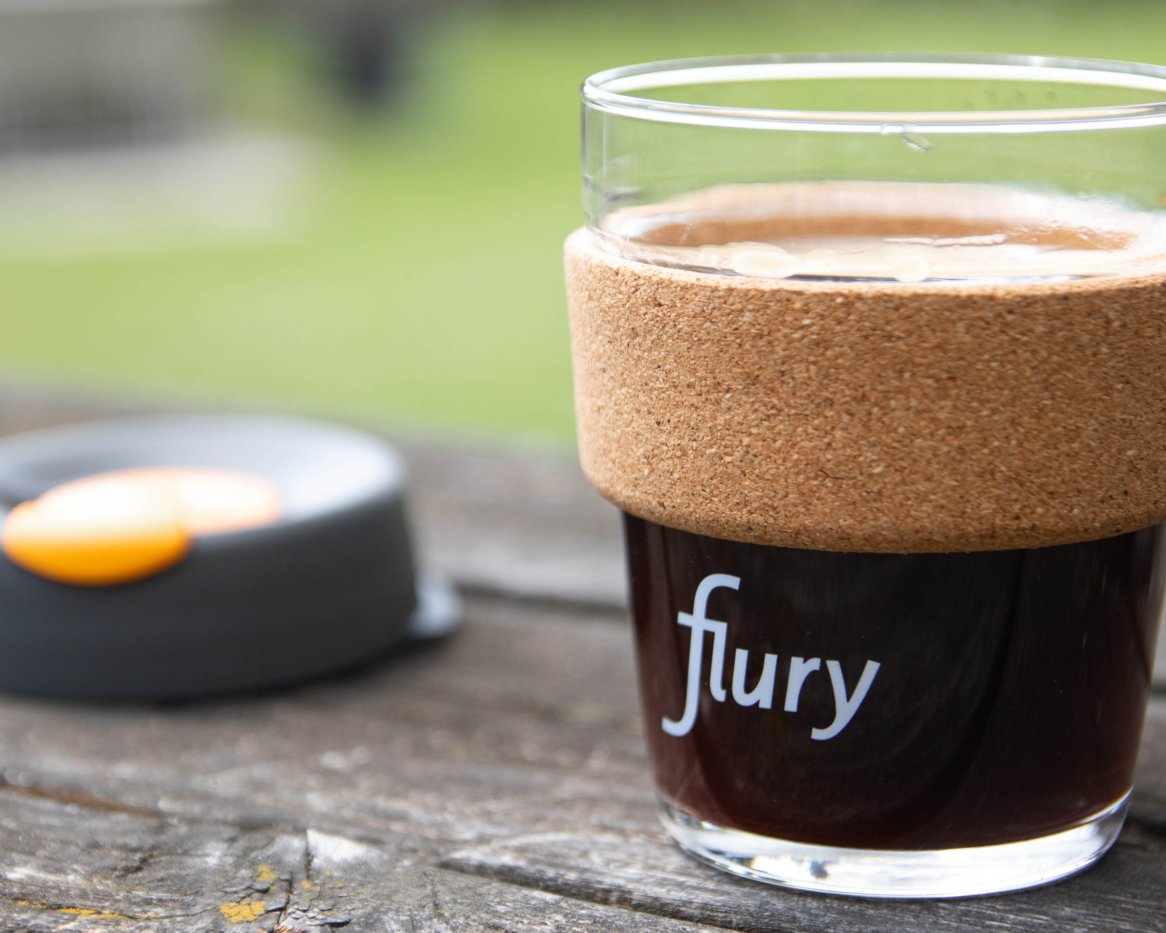 FluryCup aus Glas gefüllt mit frischem Kaffee steht auf einem Holztisch.
