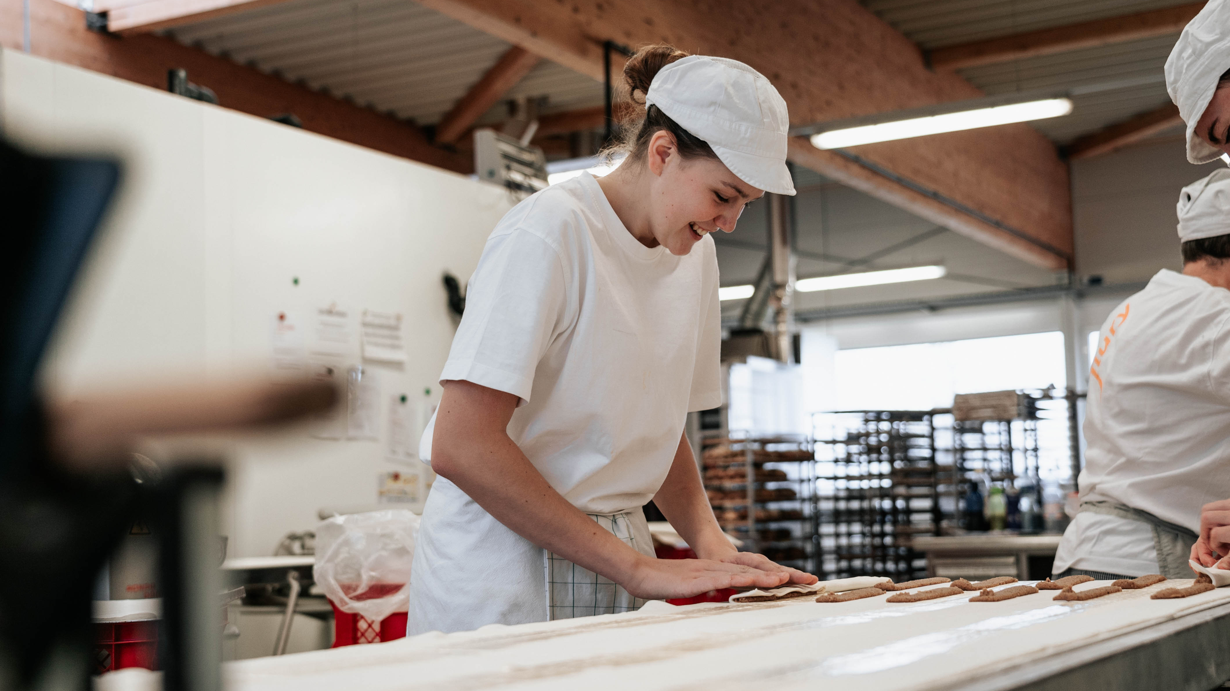 Stelleninserat Produktion_2 Bäckerin rollt eine Nussstange zusammen und lacht dabei.