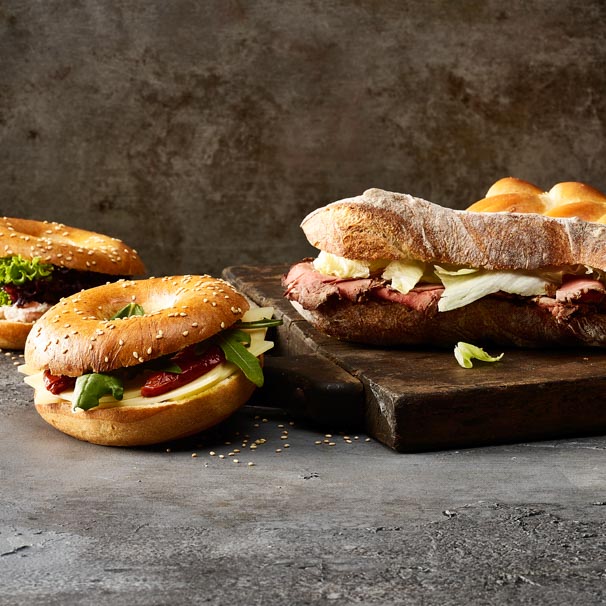 Unterschiedliche Sandwiches aus dunklem Brot mit Roastbeef oder Bagle mit Käse und getrockneten Tomaten.