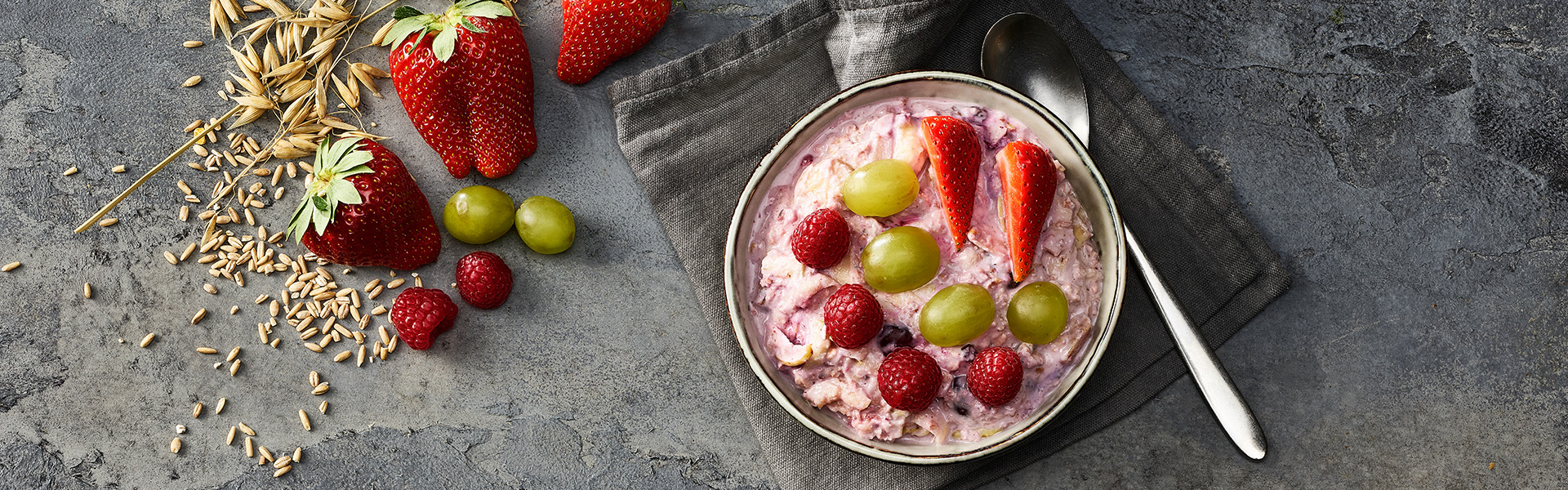 Ein Birchermüesli mit frischen Erdbeeren, Trauben und Himbeeren in einer Schale. 