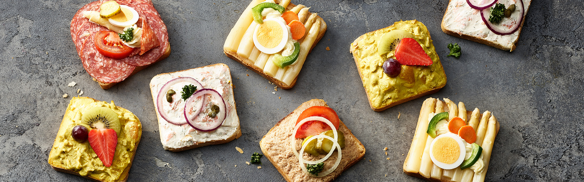 Canapés der Sorten Lachs, Thon, Salami, Spargel und Curry sind auf einem Stein präsentiert.