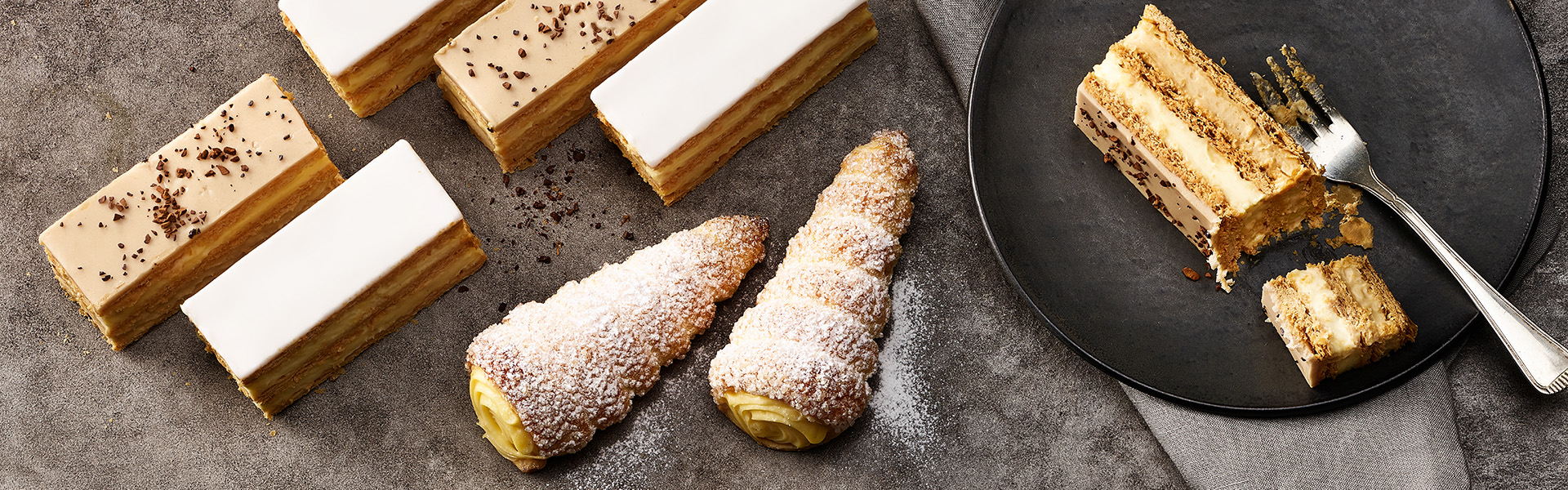 2 Sorten Cremeschnitte und Vanille Cornets sind auf einem Tisch.