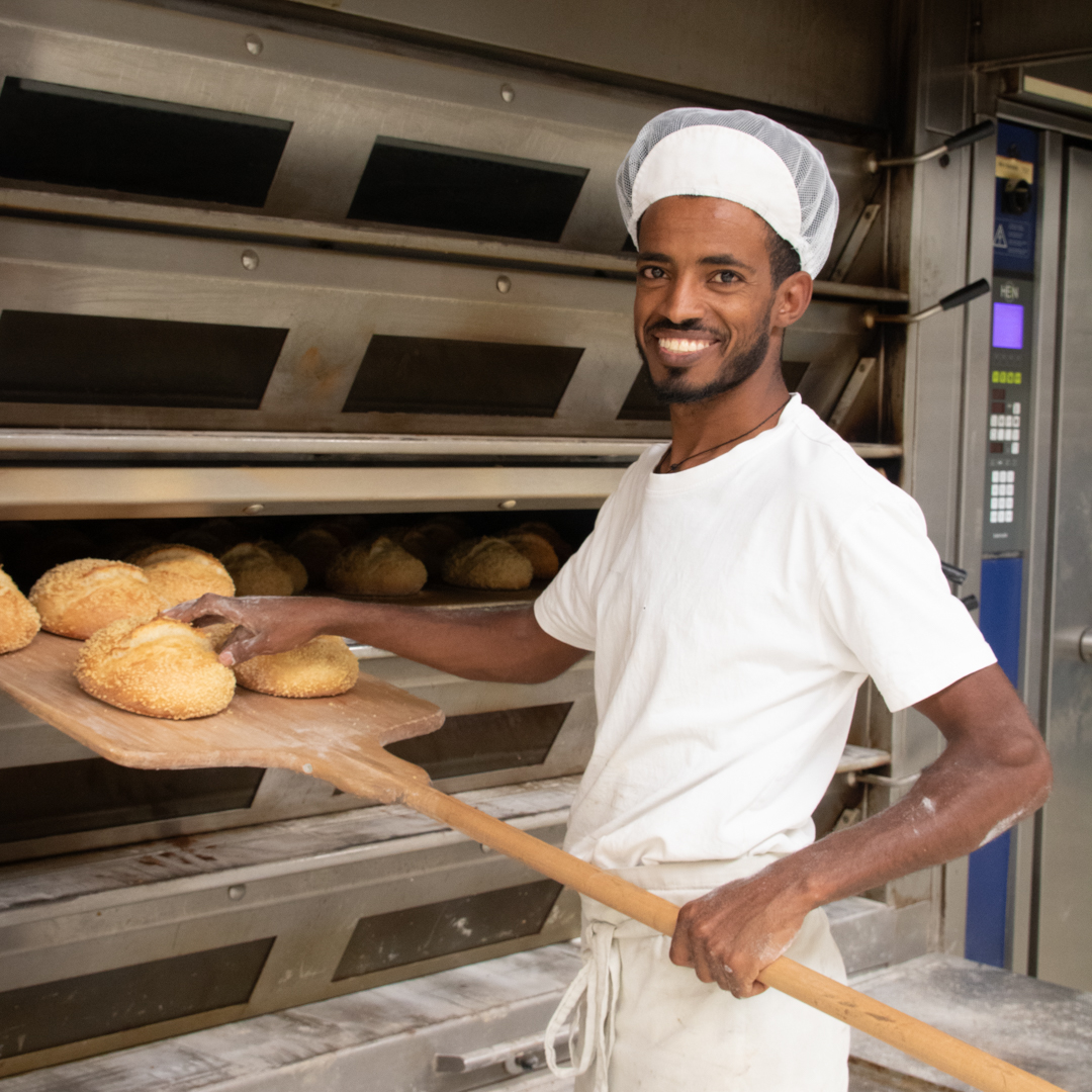 Filmon holt das frisch gebackene Maisbrot mit der Bäckerschaufel aus dem Ofen.