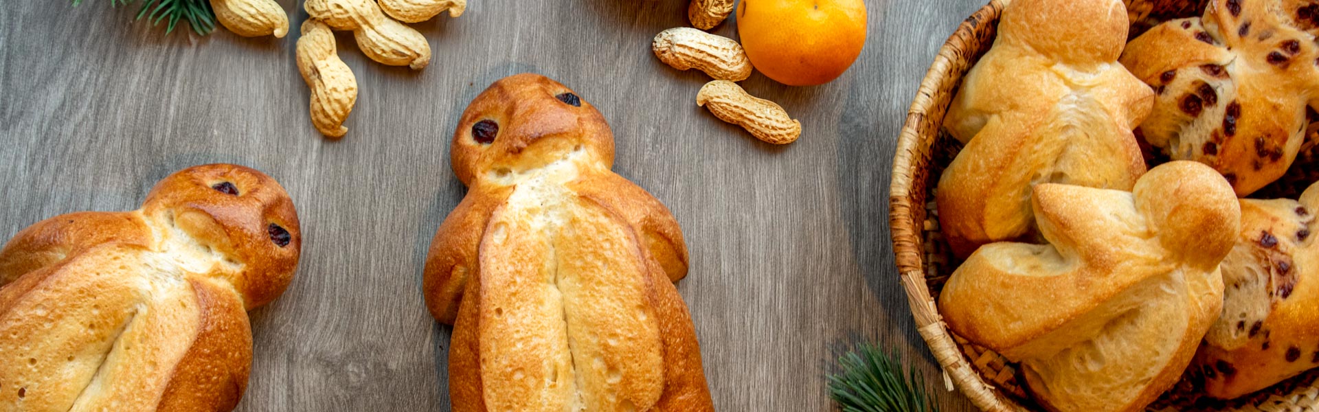Header_Grittibänz.jpg Verschiedene Grittibänzen, Mandarinen und Erdnüsse liegen auf einem festlichen Tisch verteilt.