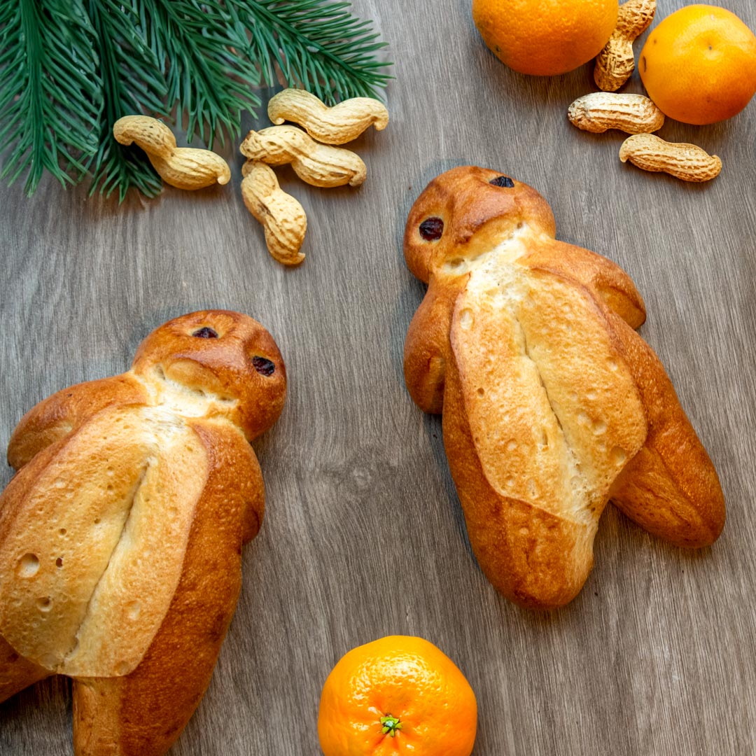 Header_Grittibänz_mobile.jpg Verschiedene Grittibänzen, Mandarinen und Erdnüsse liegen auf einem festlichen Tisch verteilt.