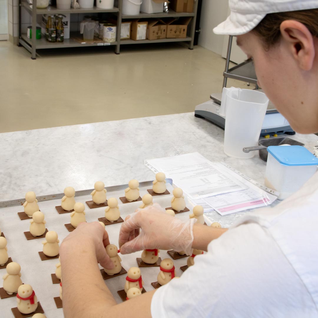 Meret zieht den Marzipanschneemännern einen roten Schal aus Marzipan an.