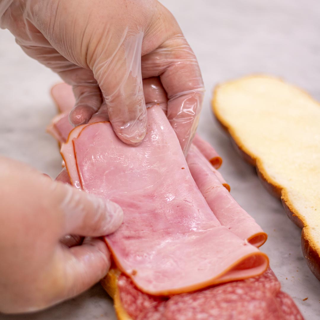 240326_Sandwich belegen.jpg Zopfbrötchen wird von Hand mit Schinken belegt.