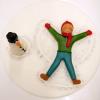 Runder Tortendecor mit Junge, der einen Schneeengel macht und daneben steht ein Schneemann aus Fondant.