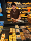 Rodrigo steht hinter der Theke, lächelt in die Kamera und nimmt ein Sandwich für den Kunden.